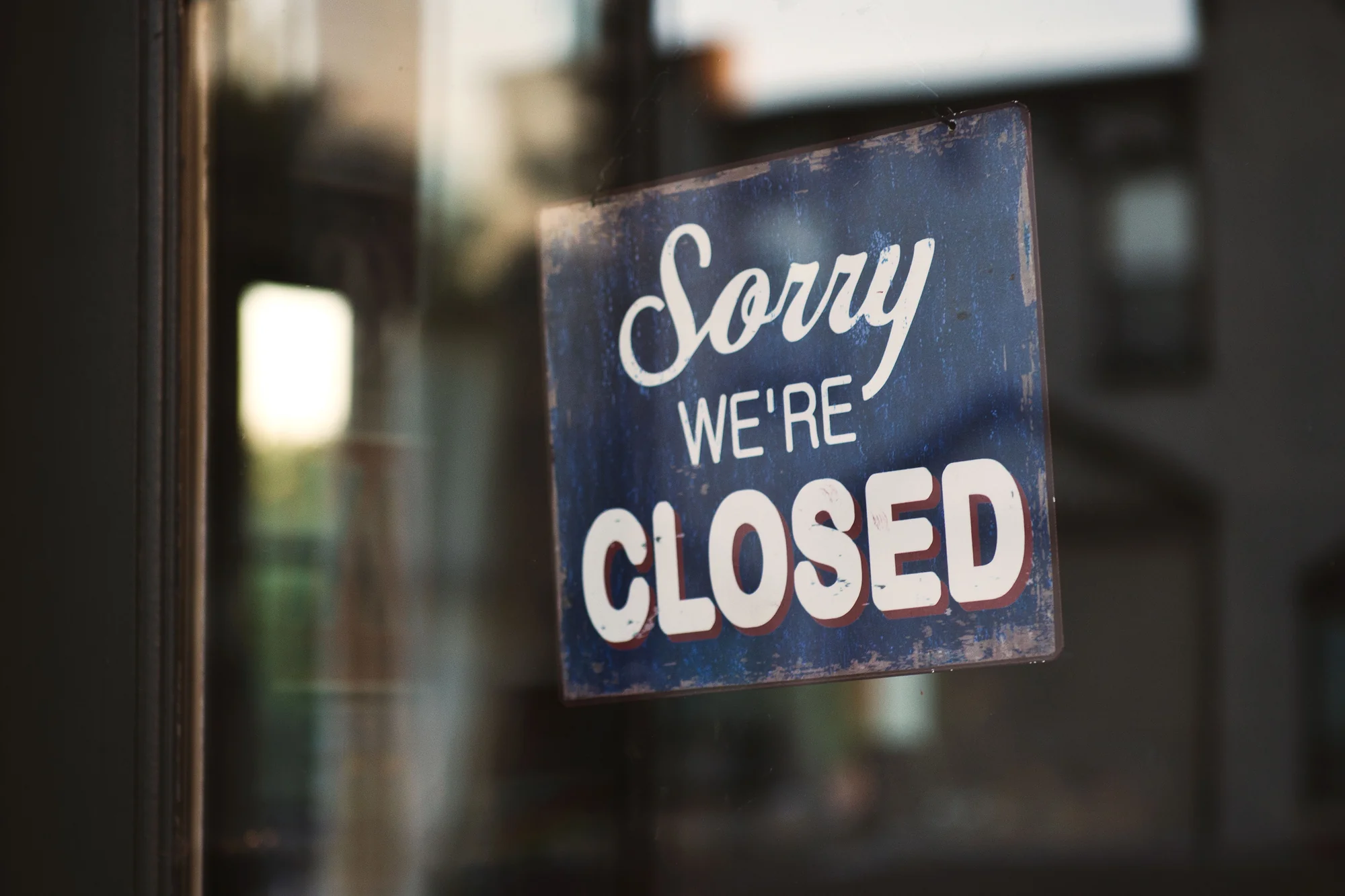 Blauw bordje “Sorry, we zijn gesloten” achter een etalageruit